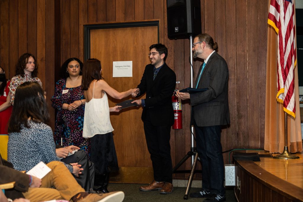 Student receives their award certificate from Professor Brandon Bloch and Undergraduate Advisor, Scott Burkhardt.