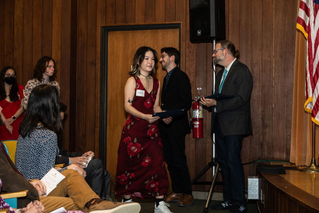 Student receives their award certificate from Professor Brandon Bloch and Undergraduate Advisor, Scott Burkhardt.