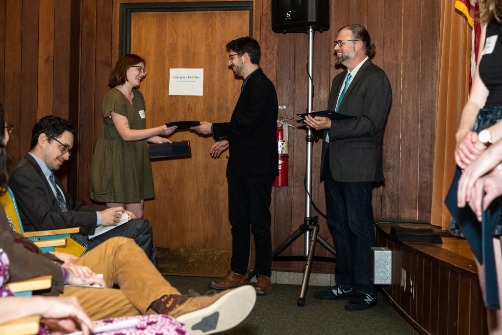 Student receives their award certificate from Professor Brandon Bloch and Undergraduate Advisor, Scott Burkhardt.