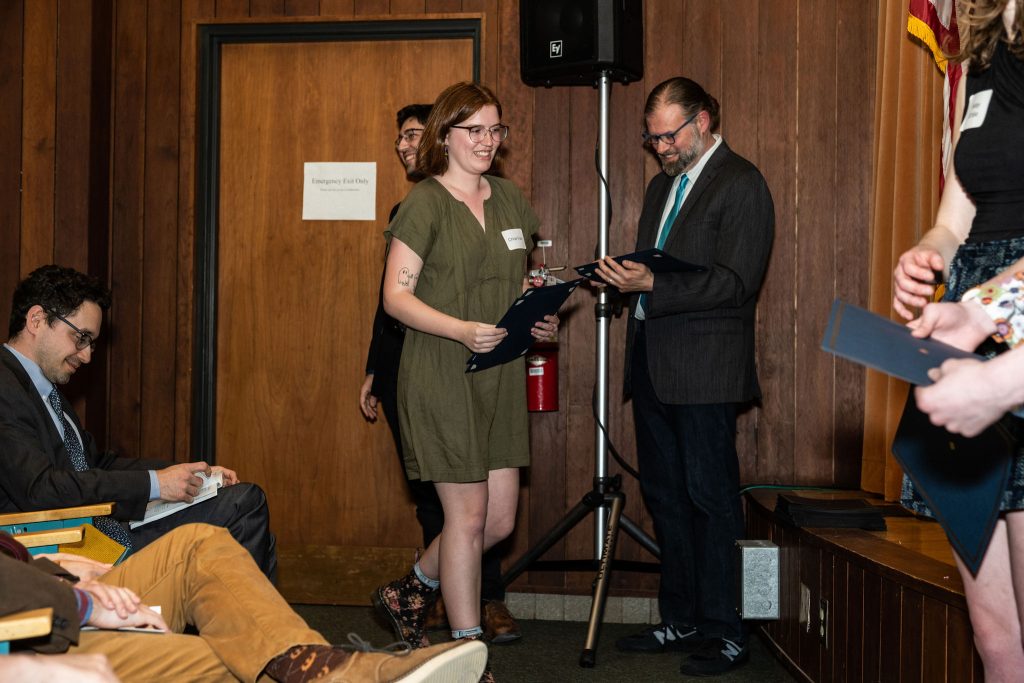 Student receives their award certificate from Professor Brandon Bloch and Undergraduate Advisor, Scott Burkhardt.