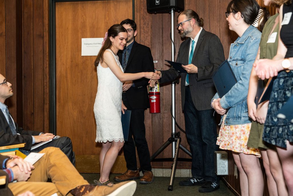 Student receives their award certificate from Professor Brandon Bloch and Undergraduate Advisor, Scott Burkhardt.