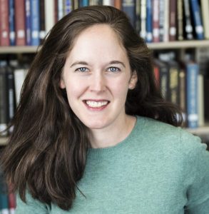 Portrait of UW-Madison History Professor Emma Kuby. The image is a headshot of Prof. Kuby, smiling in front of a bookshelf and wearing a turquoise sweater.