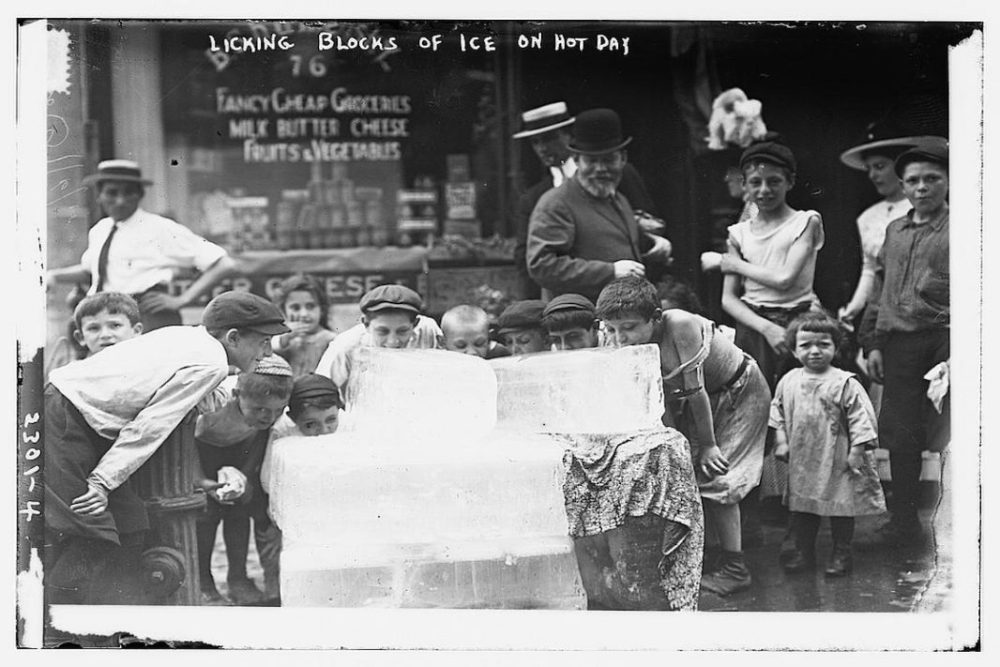 A group of children are licking large blocks of ice on a city street.