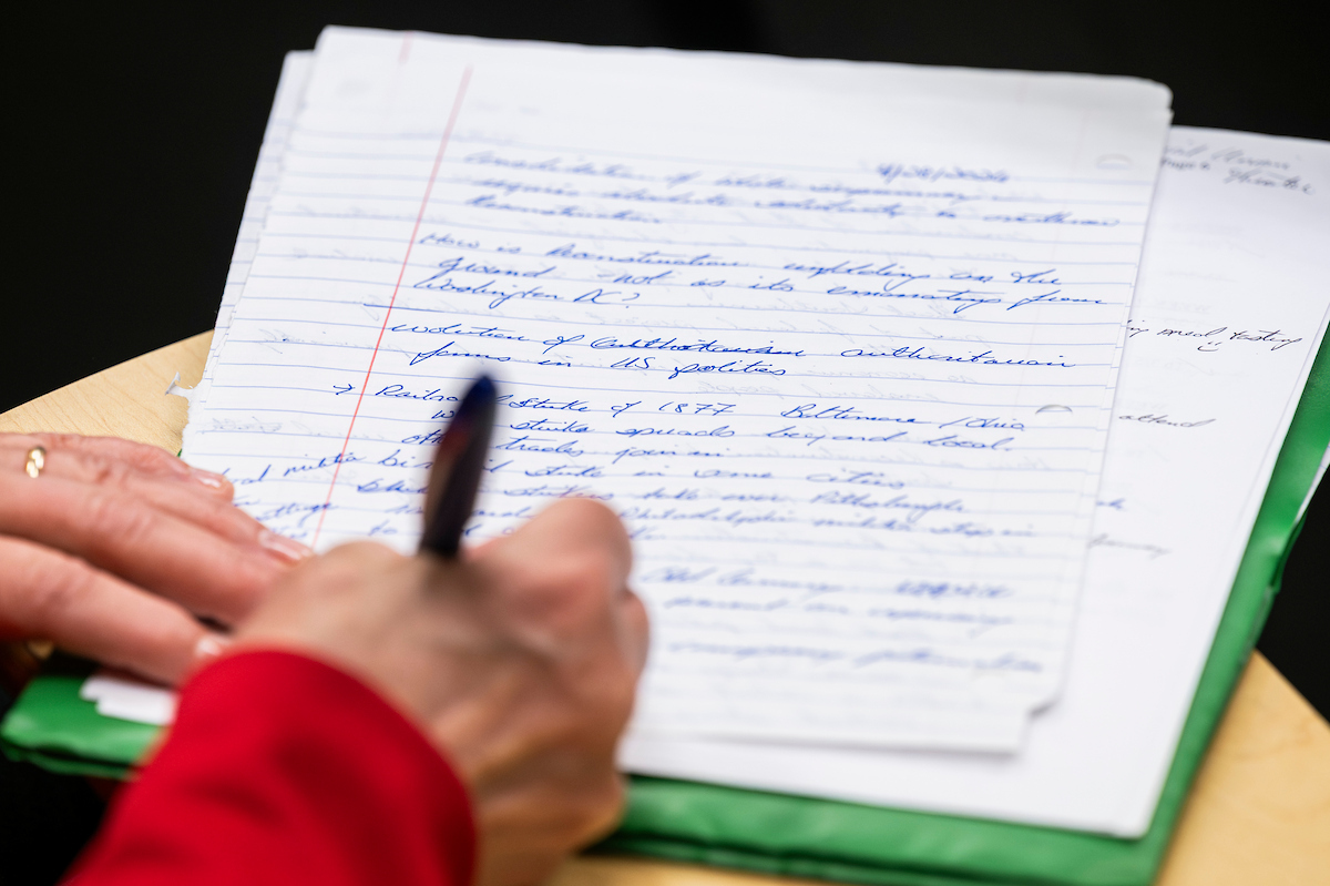 Student writing notes with a pen on notebook paper